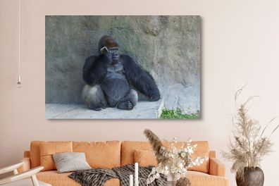 Leinwandbilder - 150x100 cm - Ein riesiger Gorilla lehnt an einer Steinmauer