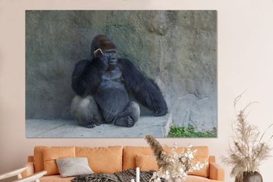 Glasbilder - 150x100 cm - Ein riesiger Gorilla lehnt an einer Steinmauer