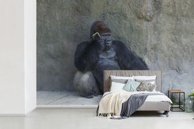 Fototapete - 600x400 cm - Ein riesiger Gorilla lehnt an einer Steinmauer