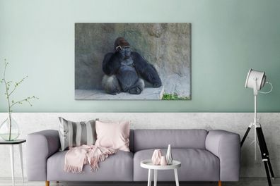 Leinwandbilder - 120x80 cm - Ein riesiger Gorilla lehnt an einer Steinmauer