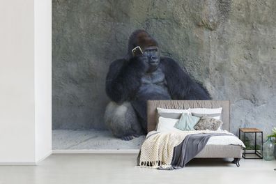 Fototapete - 525x350 cm - Ein riesiger Gorilla lehnt an einer Steinmauer